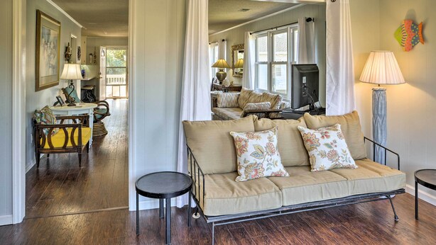 A living room with a sofa, a dining table, and a kitchen area visible through an open door. - Canalfront Surfside Beach Home - Walk to Beach! (Surfside Beach)