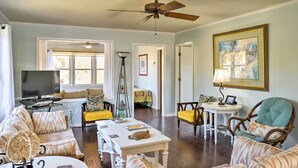 A living room with a television, sofa, chairs, a table, and a ceiling fan. - Canalfront Surfside Beach Home - Walk to Beach! (Surfside Beach)