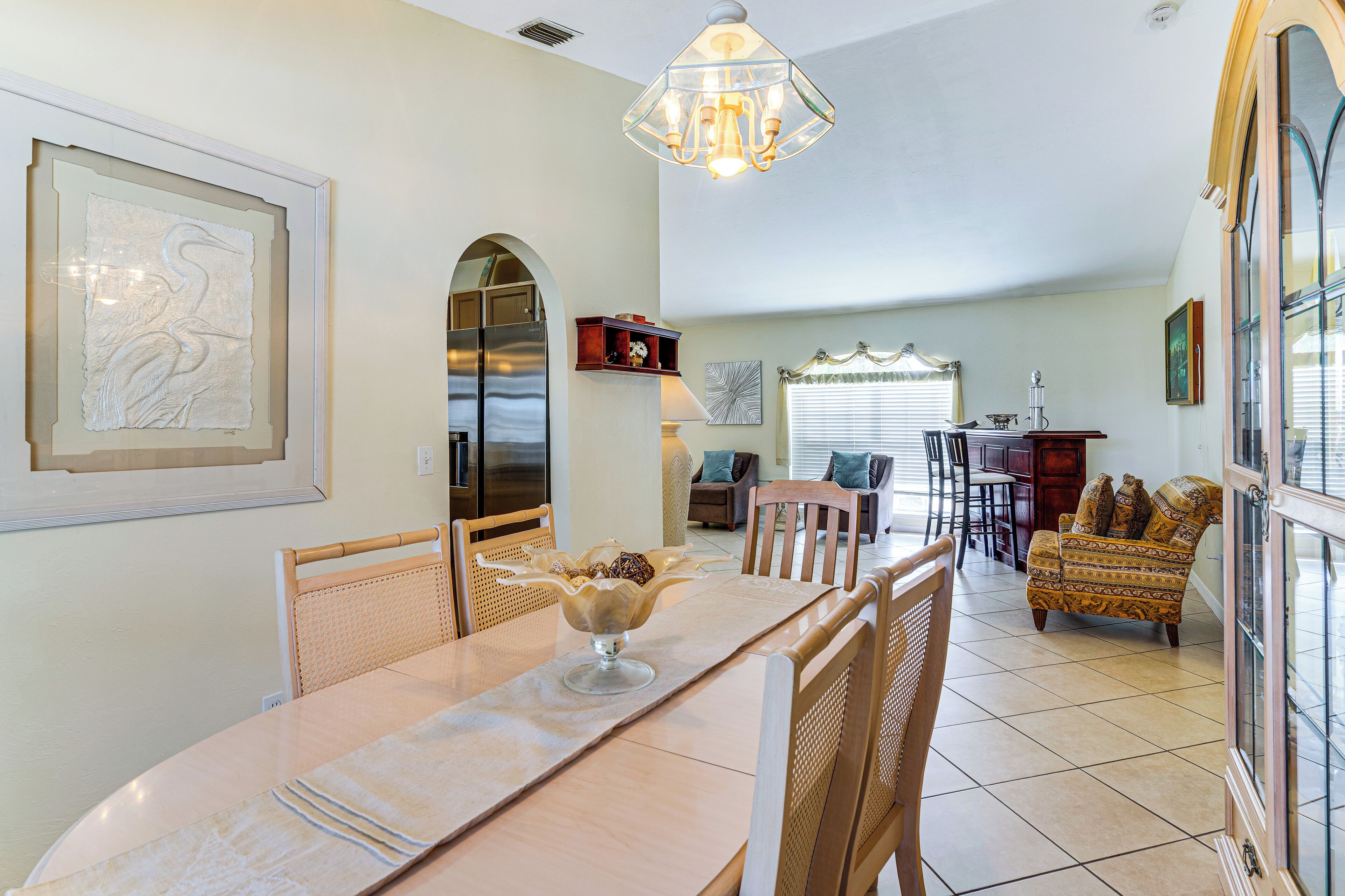 A dining area with a table, chairs, and a chandelier. There is a sofa and a cabinet in the background.