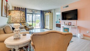 Ein Wohnzimmer mit Sofa, Sesseln, Lampe, Fernseher und Blick ins Freie.