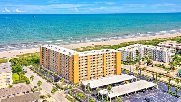 Ein Hotel mit mehreren Etagen, einem Parkplatz und Blick auf den Strand.
