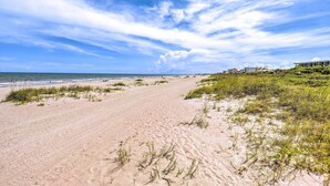 Ein Sandstrand mit Dünen und blauem Himmel.