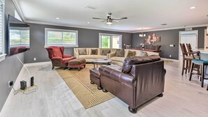 A spacious living room with a large sofa, a red armchair, and a dining area with wooden chairs and a table. - 3 Mi to Dtwn Bradenton: Home w/ Yard! (Bradenton)