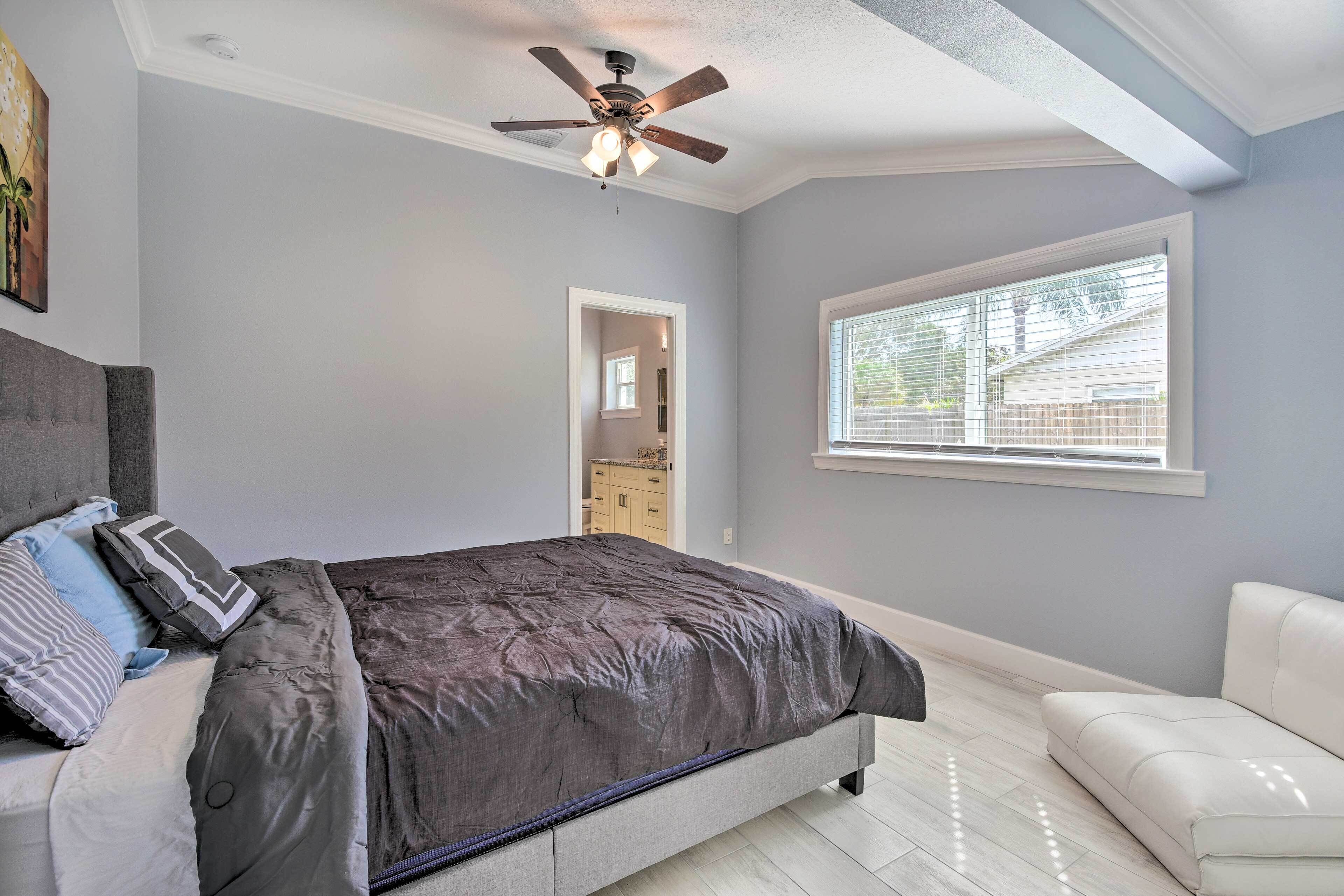 A bedroom with a bed, a ceiling fan, a window, and a door leading to a bathroom.