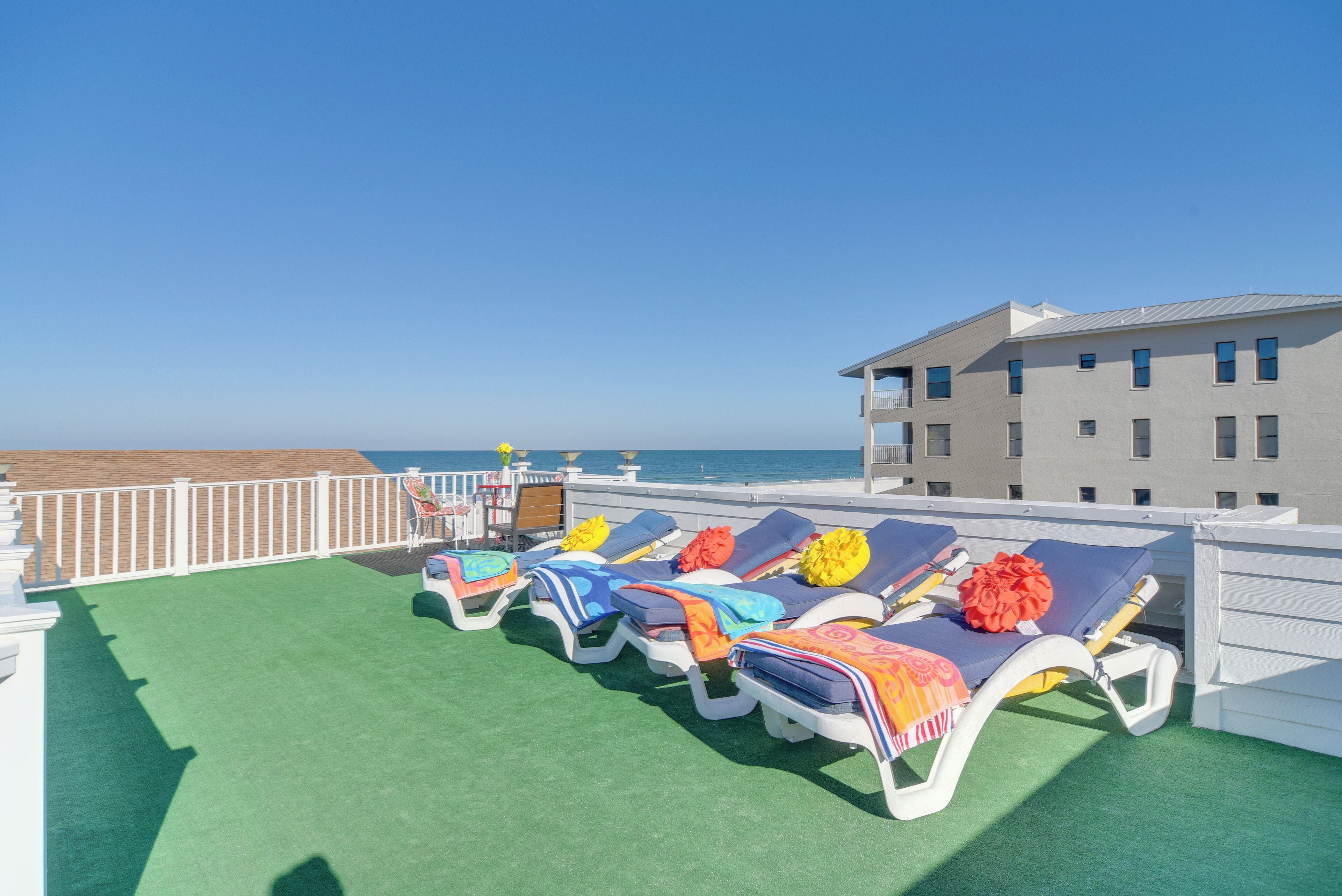 Une terrasse avec des chaises longues, une clôture blanche et un bâtiment doté de nombreuses fenêtres.