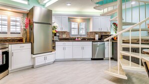 A modern kitchen with white cabinets, stainless steel appliances, and a spiral staircase. - Breezy White Sands House Steps to Gulf Shore! (Clearwater Beach)