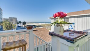 A balcony with a view of the beach, a wooden chair, a vase with red flowers, and a tray with a glass and a polka-dotted cup. - Breezy White Sands House Steps to Gulf Shore! (Clearwater Beach)