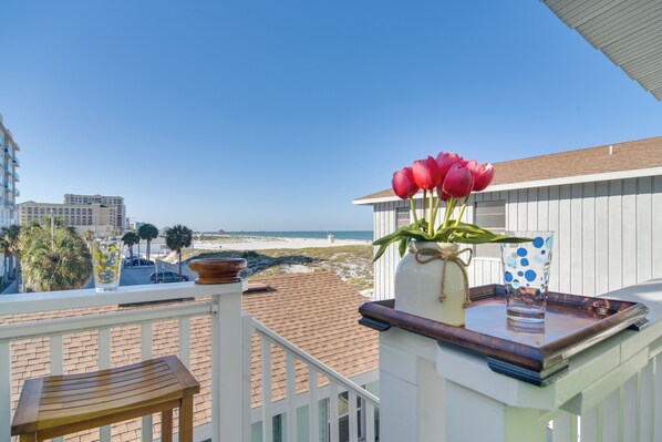 A balcony with a view of the beach, a vase with red flowers, and a glass with blue polka dots.