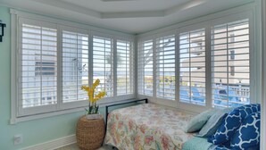 A bedroom with a large bay window, a bed with a floral bedspread, and a wicker basket with yellow flowers. - Breezy White Sands House Steps to Gulf Shore! (Clearwater Beach)