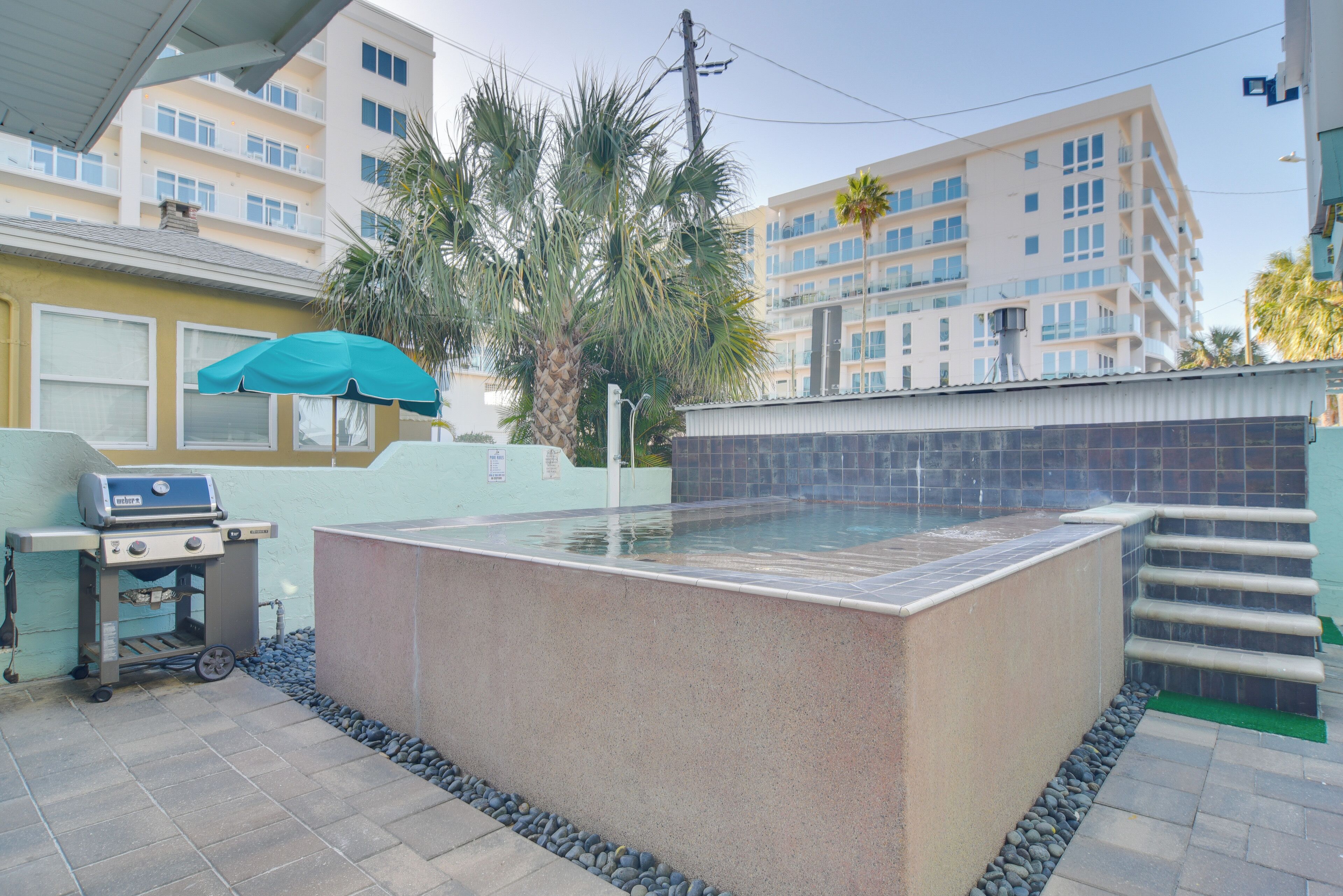 A rectangular hot tub with a tiled surround, a grill, and a palm tree in the background.
