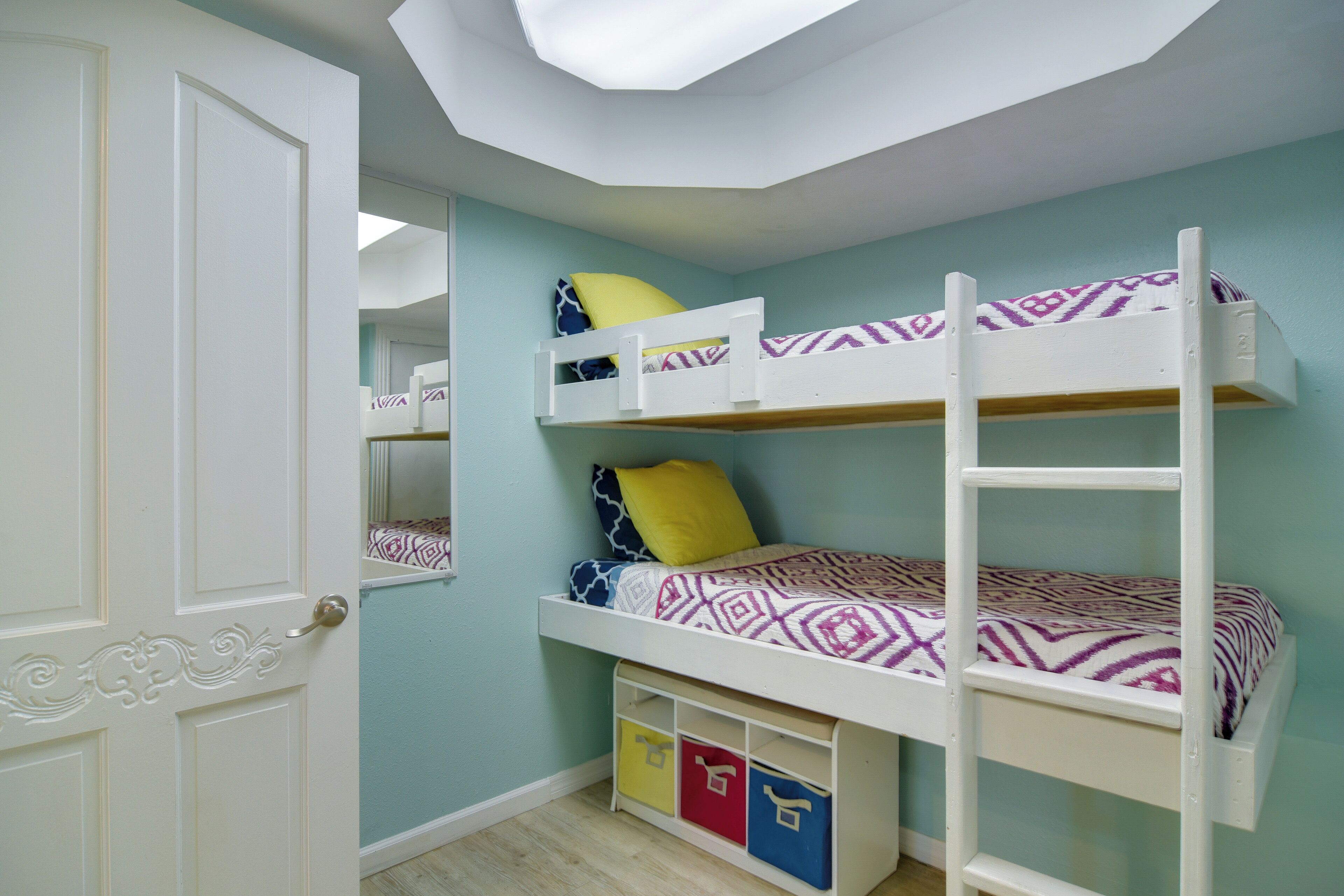 A bunk bed with patterned bedding, a ladder, and storage boxes under the bed.