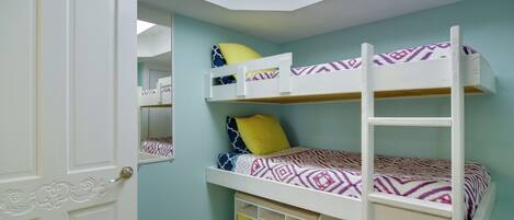 A bunk bed with patterned bedding, a ladder, and storage boxes under the bed.