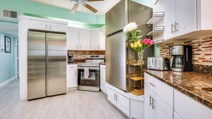 A modern kitchen with stainless steel appliances, white cabinets, and a granite countertop. - Breezy White Sands House Steps to Gulf Shore! (Clearwater Beach)