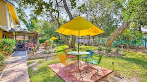 A patio with a table and chairs, surrounded by greenery and a yellow umbrella. - Brandon Vacation Rental Home w/ Spacious Yard (Brandon)