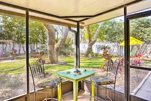 Un invernadero con una mesa y sillas, rodeado de paredes de vidrio y vistas a un jardín.