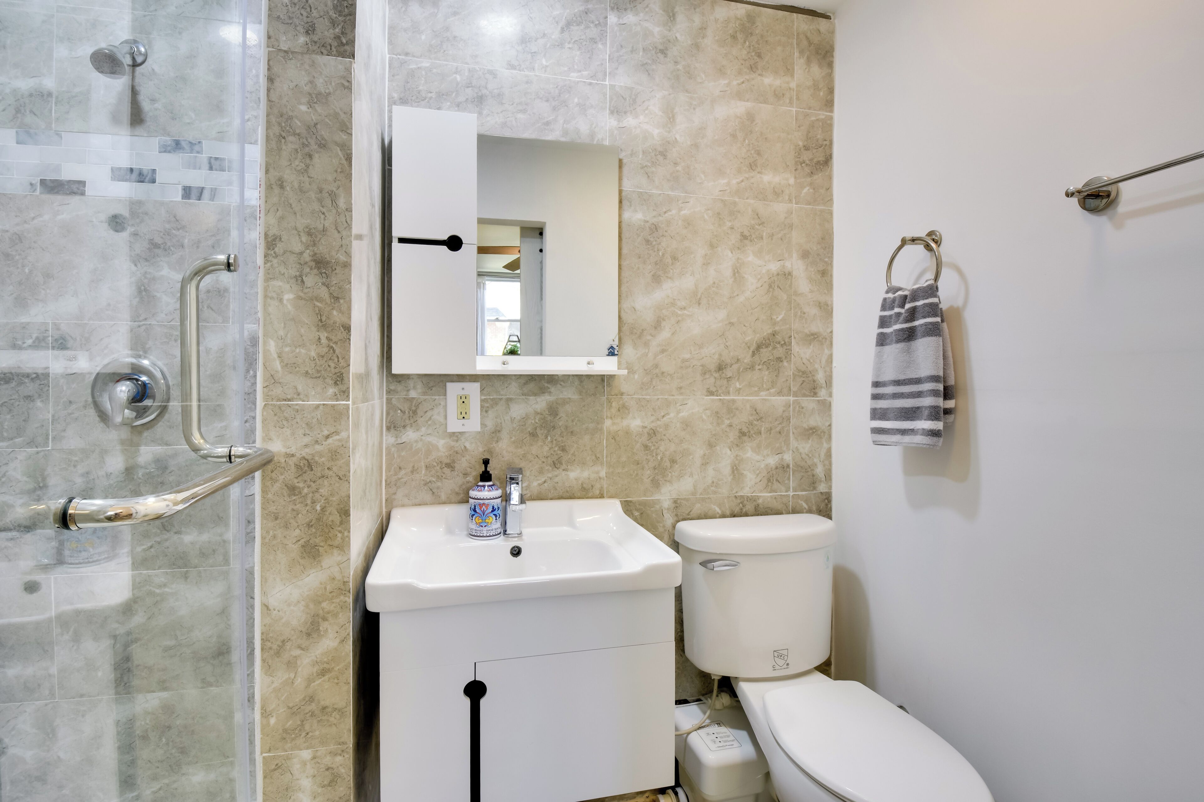 A bathroom with a glass shower enclosure, a white sink with a mirror above it, and a toilet.