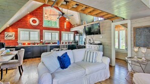 A cozy living room with a white sofa, a dining table, and a kitchen area with wooden beams and a red accent wall.