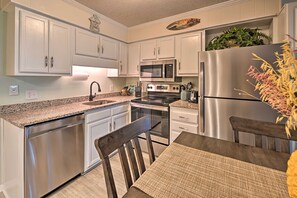 A modern kitchen with white cabinets, stainless steel appliances, and a dining area with a wooden table and chairs.
