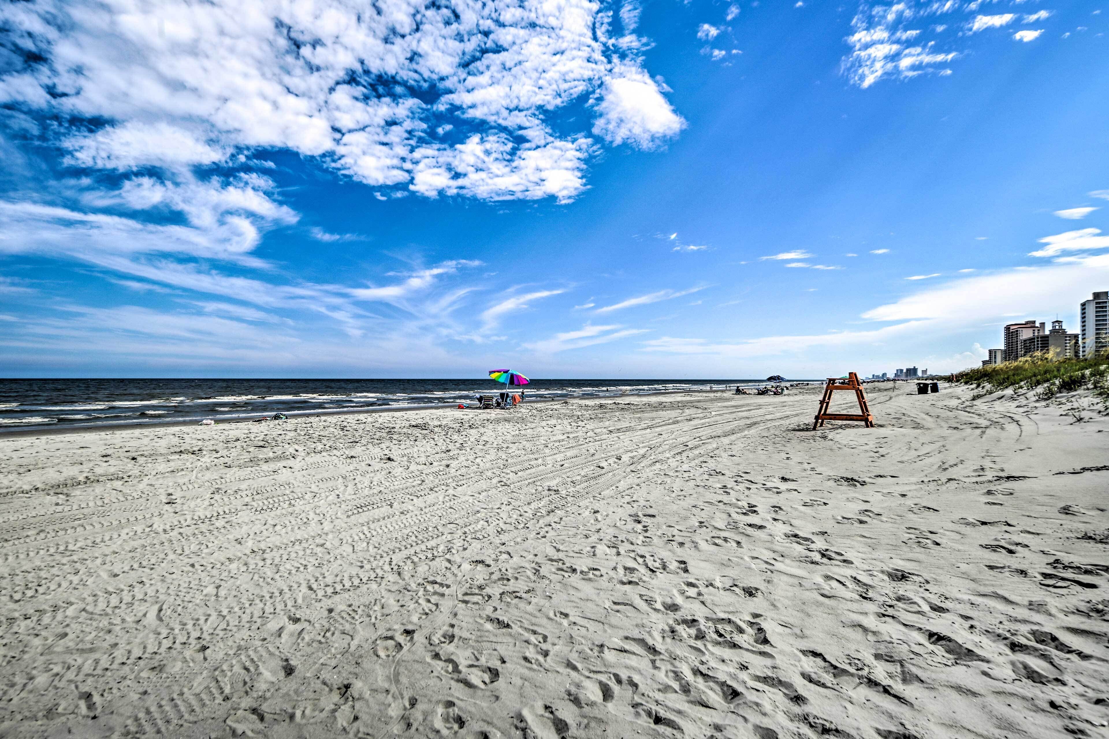A sandy beach with footprints, a colorful umbrella, and a lifeguard stand.
