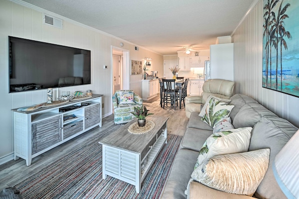 A living room with a TV, a sofa, a coffee table, and a dining area with chairs and a table. - Myrtle Beach Condo w/ On-site Pool & Beach Access (Myrtle Beach)