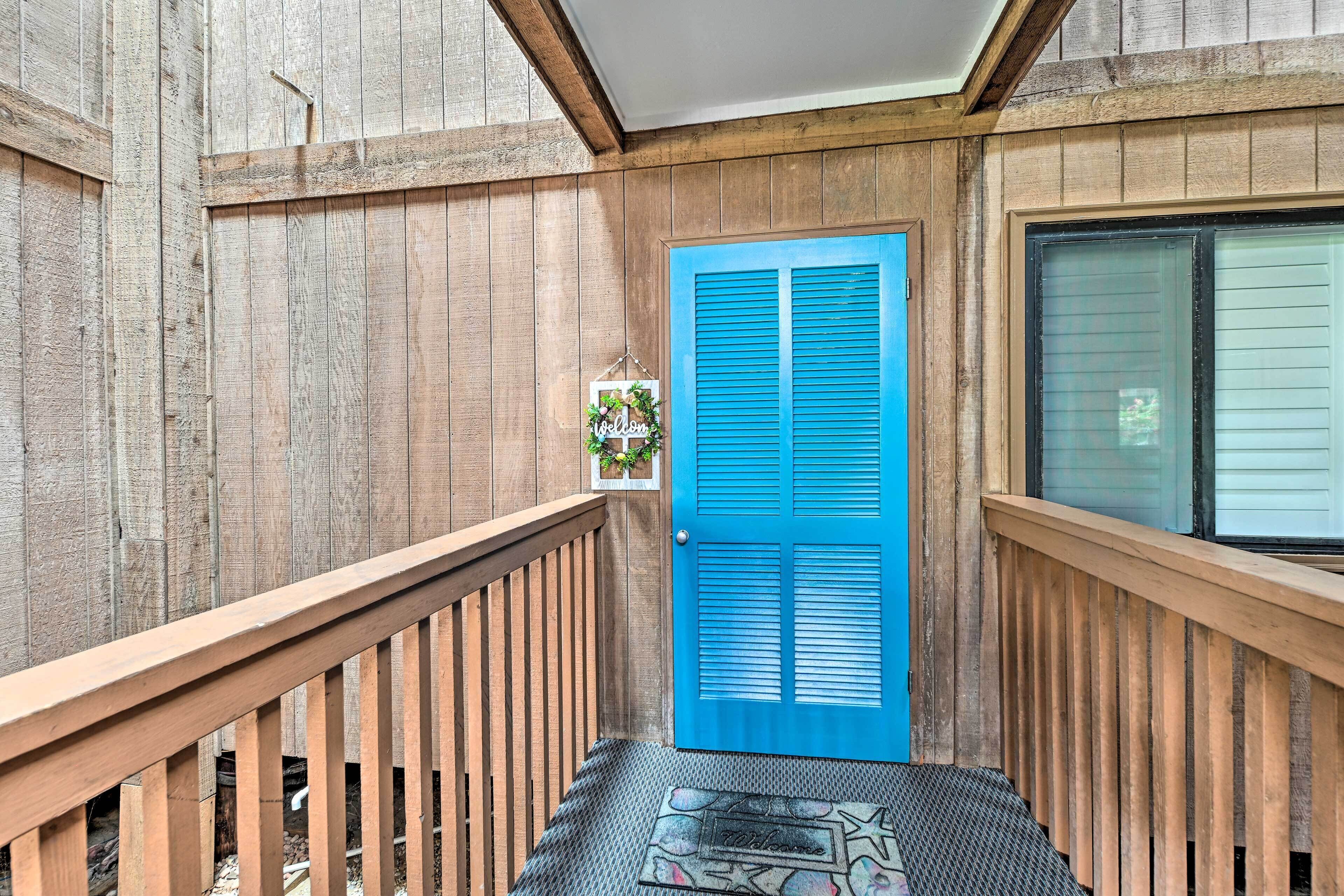 Ein Holzbalkon mit blauer Tür, einem Willkommensschild und einer Fußmatte.