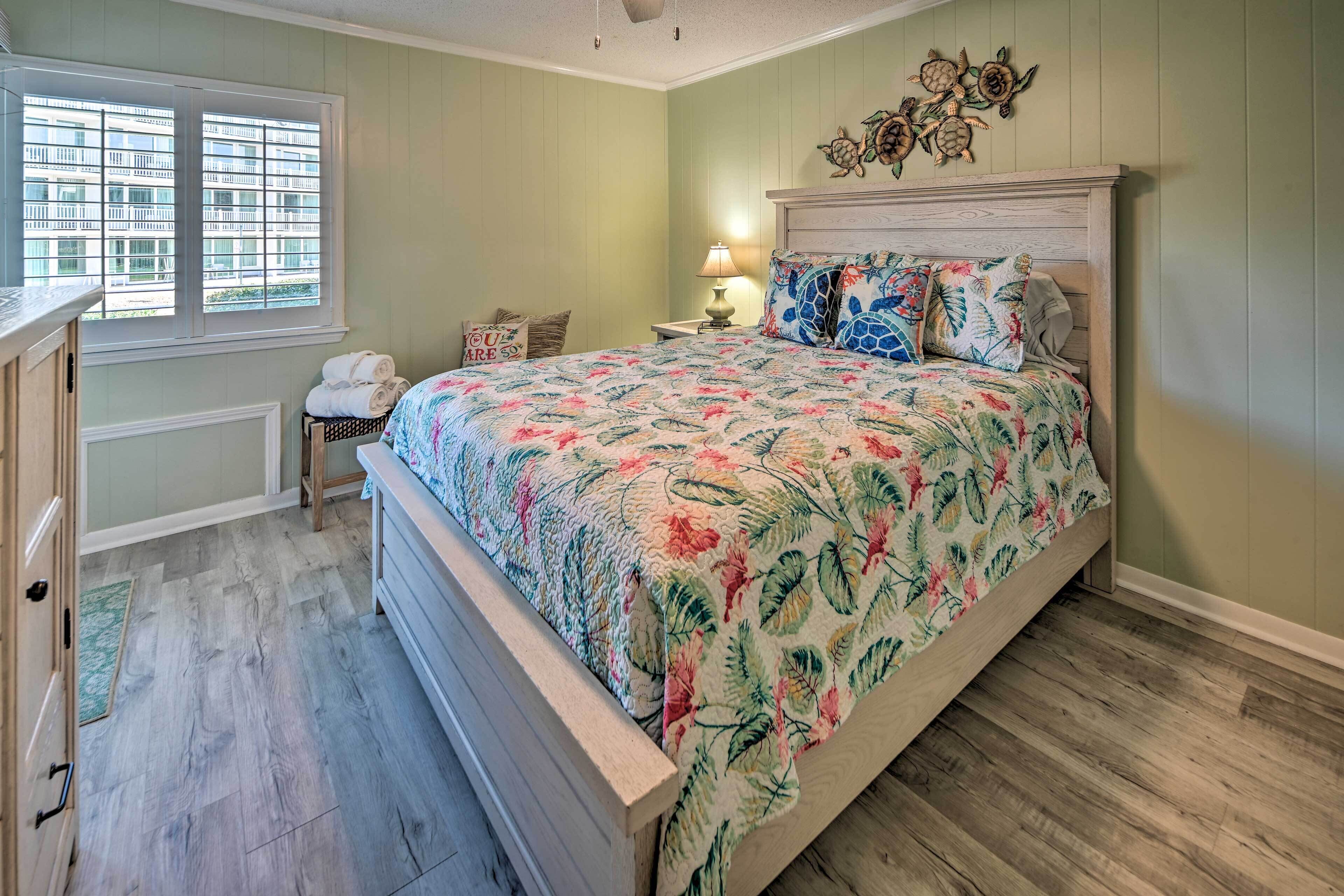 A bedroom with a bed, a nightstand, a lamp, a window with blinds, and a door.