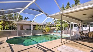 Ein überdachter Pool mit Liegestühlen und einem Tisch, umgeben von einer Metallkonstruktion und Glasplatten.