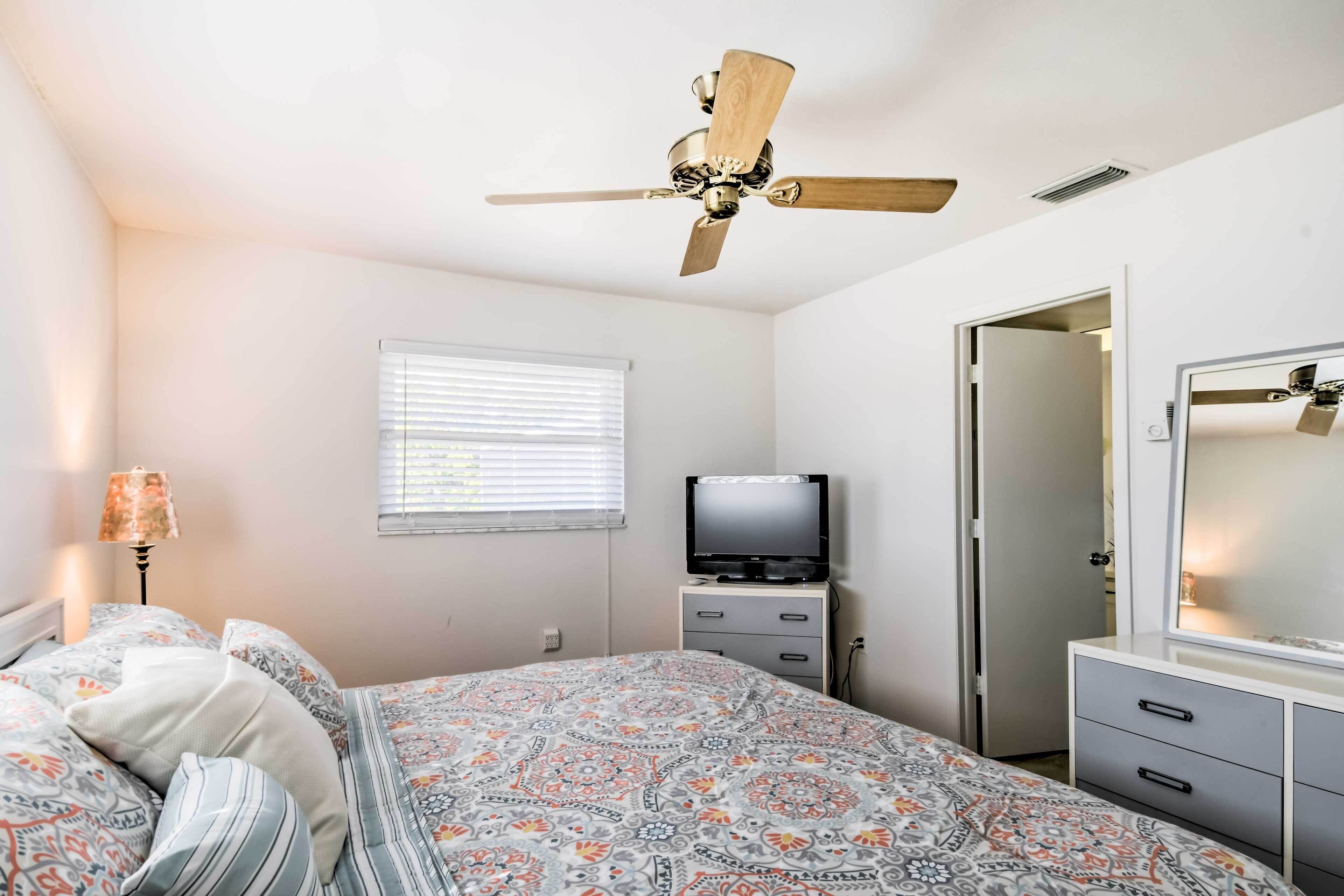 Un dormitorio con cama, ventilador de techo, televisor, cómoda y espejo.