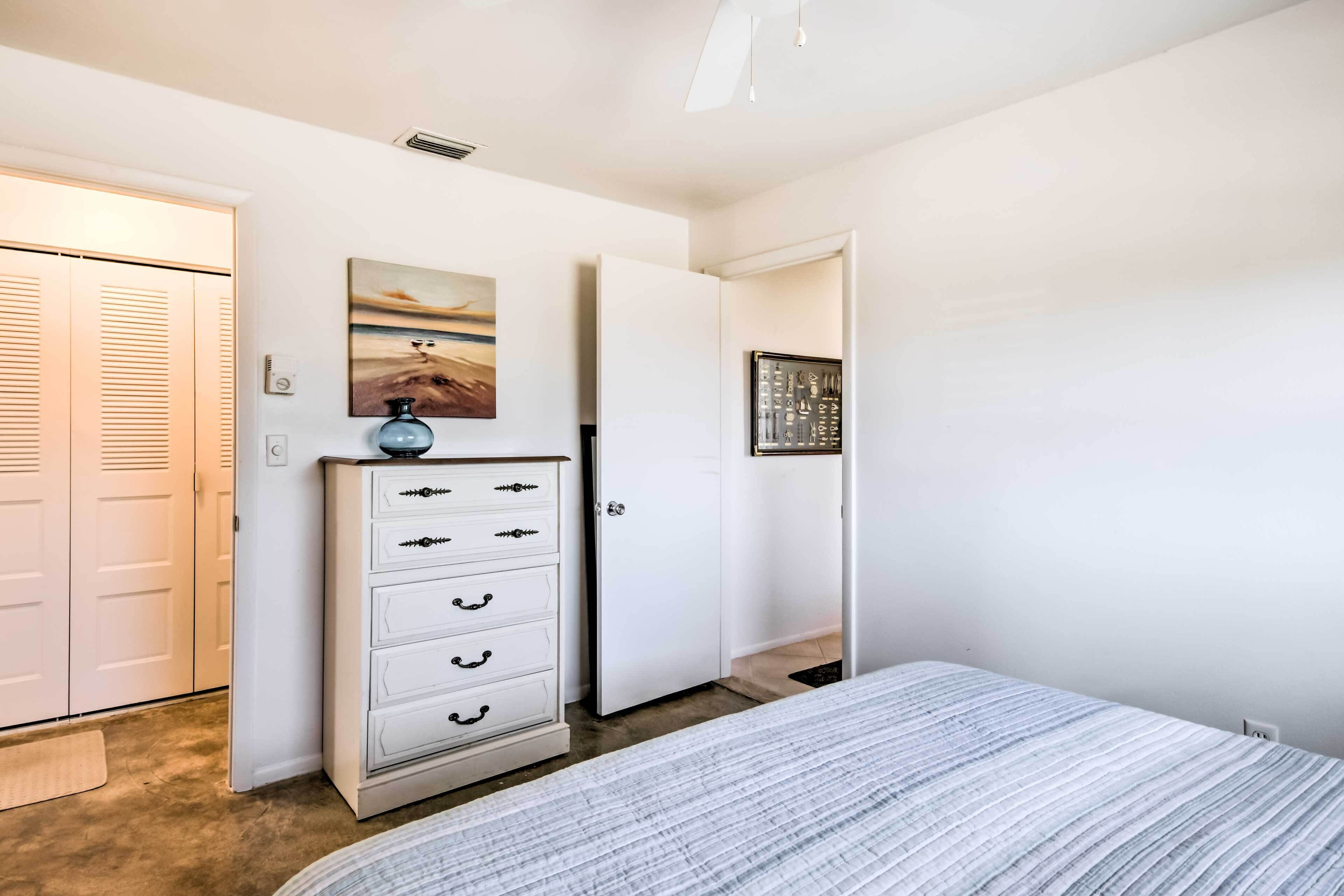 A bedroom with a bed, a dresser, a door, and a wall with a painting.