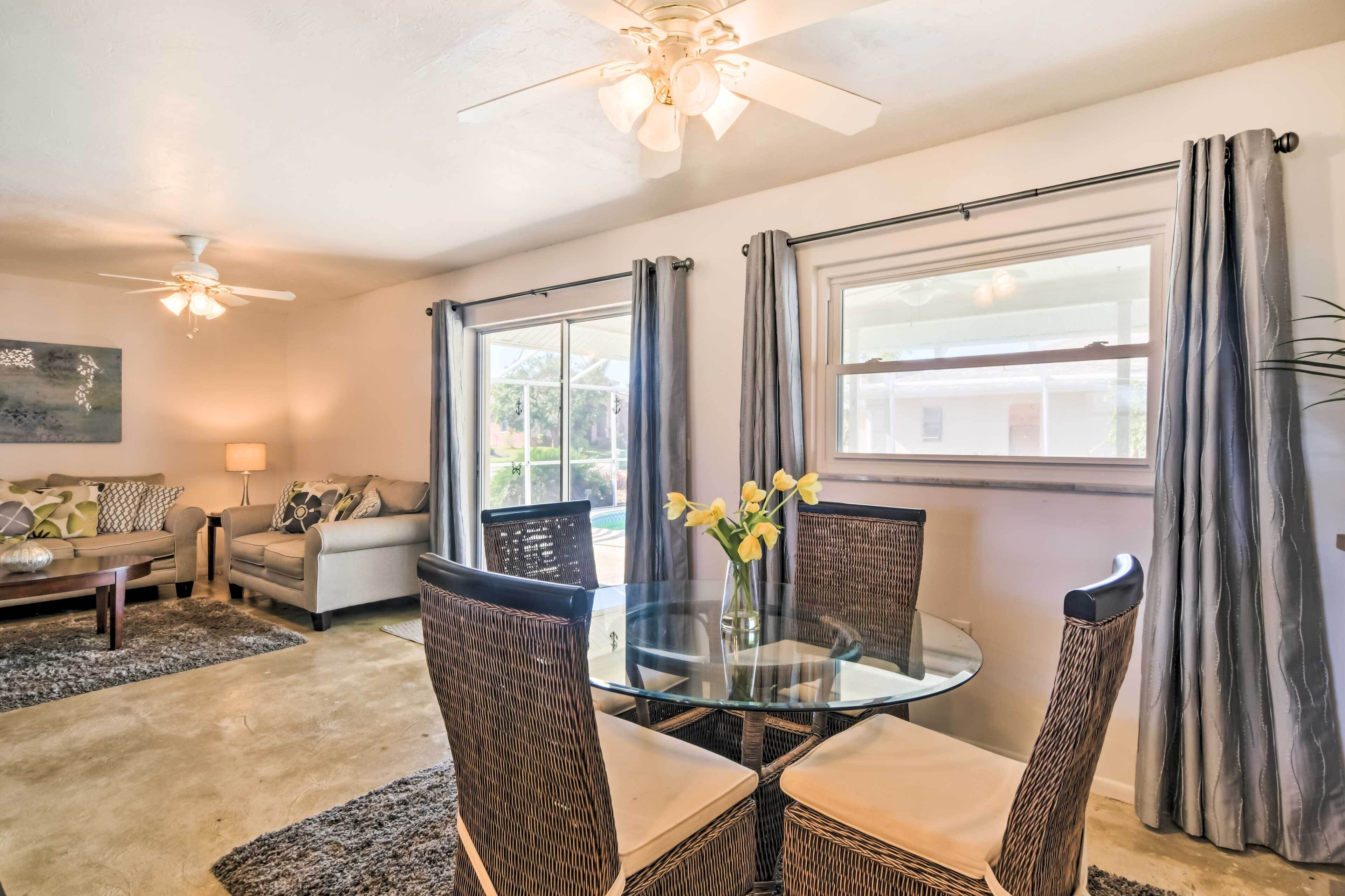 A living room with a glass-top table, wicker chairs, a sofa, and a ceiling fan.