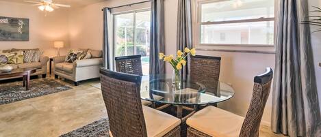 A living room with a glass-top table, wicker chairs, a sofa, and a ceiling fan.