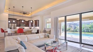 A spacious living area with a large sectional sofa, a glass coffee table, and a view of a swimming pool through large sliding glass doors. - Cape Coral Getaway w/ Private Outdoor Pool! (Cape Coral)