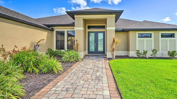 A modern house with a brick pathway leading to a dark entrance, surrounded by well-maintained landscaping. - Cape Coral Getaway w/ Private Outdoor Pool! (Cape Coral)