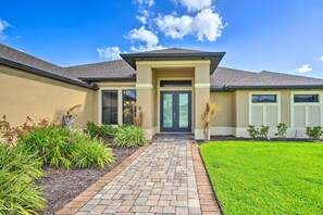 A modern house with a brick pathway leading to a dark entrance, surrounded by well-maintained landscaping. - Cape Coral Getaway w/ Private Outdoor Pool! (Cape Coral)