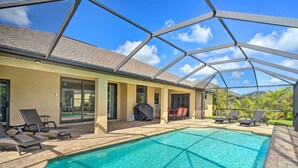 A swimming pool with lounge chairs, a covered grill, and a glass-enclosed patio. - Cape Coral Getaway w/ Private Outdoor Pool! (Cape Coral)