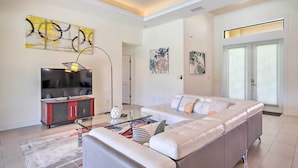 A modern living room with a large sectional sofa, a flat-screen TV, and artwork on the walls. - Cape Coral Getaway w/ Private Outdoor Pool! (Cape Coral)