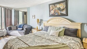 A hotel room with a large bed, a sofa, a bedside table with a lamp, and a window with curtains. - Caravelle Tower Condo Rental: Walk to Beach (Myrtle Beach)