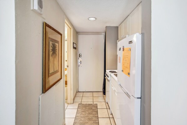 A narrow hallway with a tiled floor, a refrigerator, a stove, and a door at the end. - Caravelle Tower Condo Rental: Walk to Beach (Myrtle Beach)