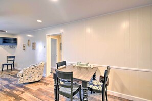 A dining area with a wooden table and four chairs, a television mounted on the wall, and a door leading to another room.