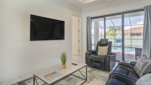 Una sala de estar moderna con un televisor de pantalla plana, un sofá de cuero y un ventanal con vistas a una piscina.