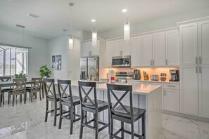 A modern kitchen with white cabinets, a central island with bar stools, stainless steel appliances, and pendant lighting. - Cape Coral Home w/ Screened-in Lanai + Pool! (Cape Coral)
