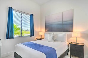A neatly made bed with a blue blanket, two bedside lamps, a nightstand, and a large abstract painting on the wall. - Cape Coral Home w/ Screened-in Lanai + Pool! (Cape Coral)