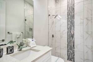 A modern bathroom with a marble vanity, a glass shelf, and a shower with a mosaic tile wall. - Cape Coral Home w/ Screened-in Lanai + Pool! (Cape Coral)