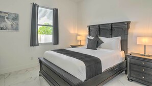 Un dormitorio con una cama de madera oscura, ropa de cama blanca, una mesita de noche con una lámpara y una ventana con cortinas.