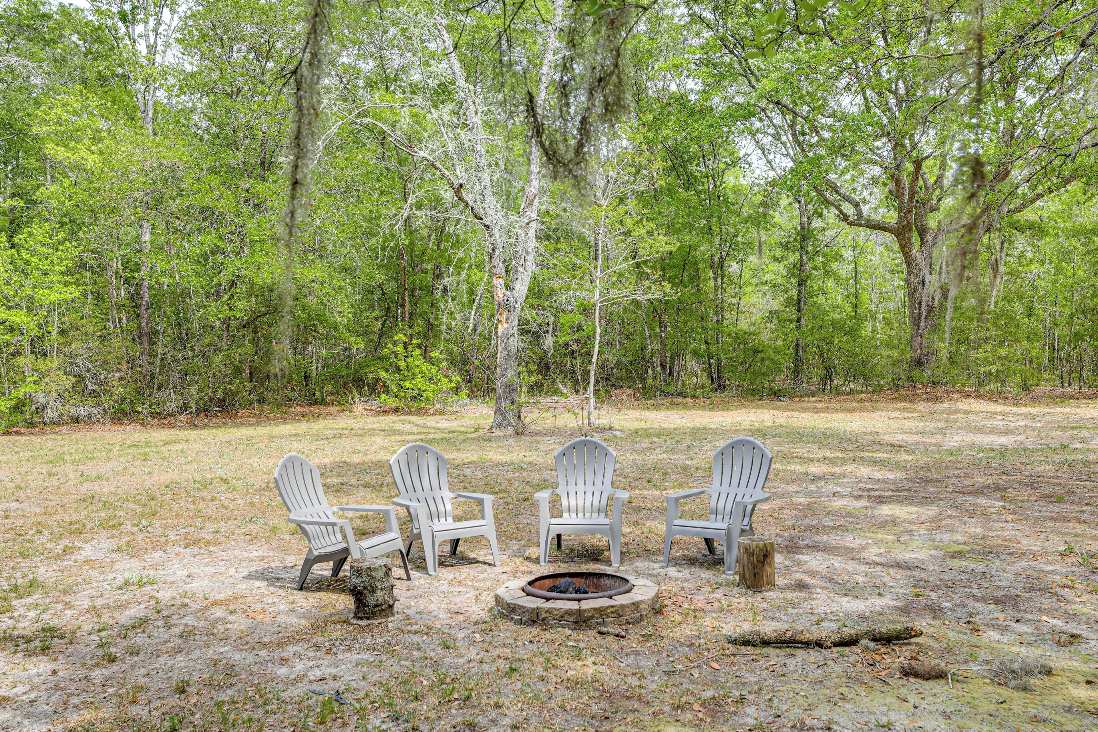A campsite with three Adirondack chairs around a fire pit in a wooded area.