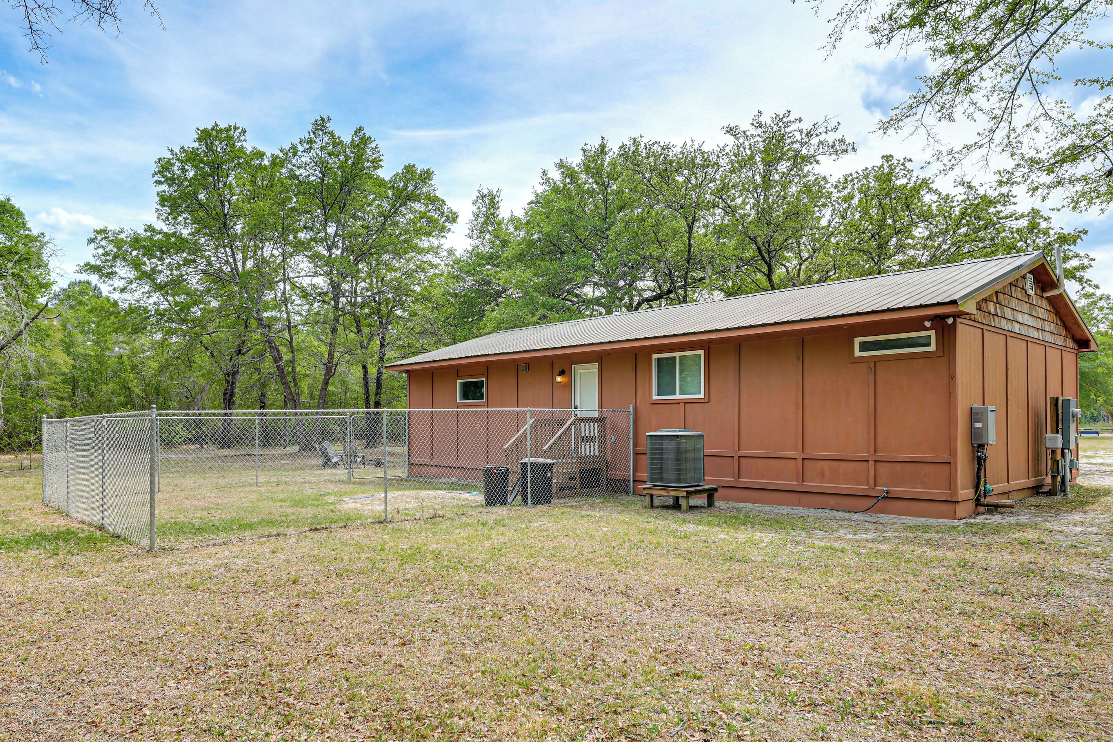 A small, single-story building with a metal roof, a fenced area, and a bench.