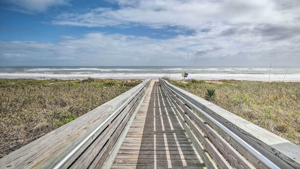 Een houten looppad dat naar een strand leidt, onder een heldere lucht.