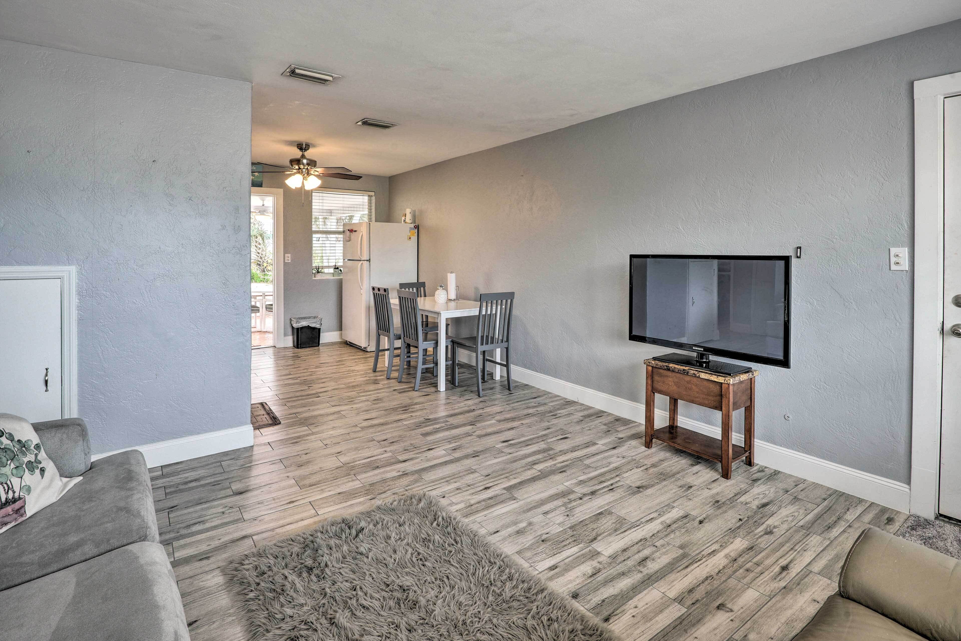 A living room with a gray couch, a TV on a wooden stand, and a dining area with a table and chairs.