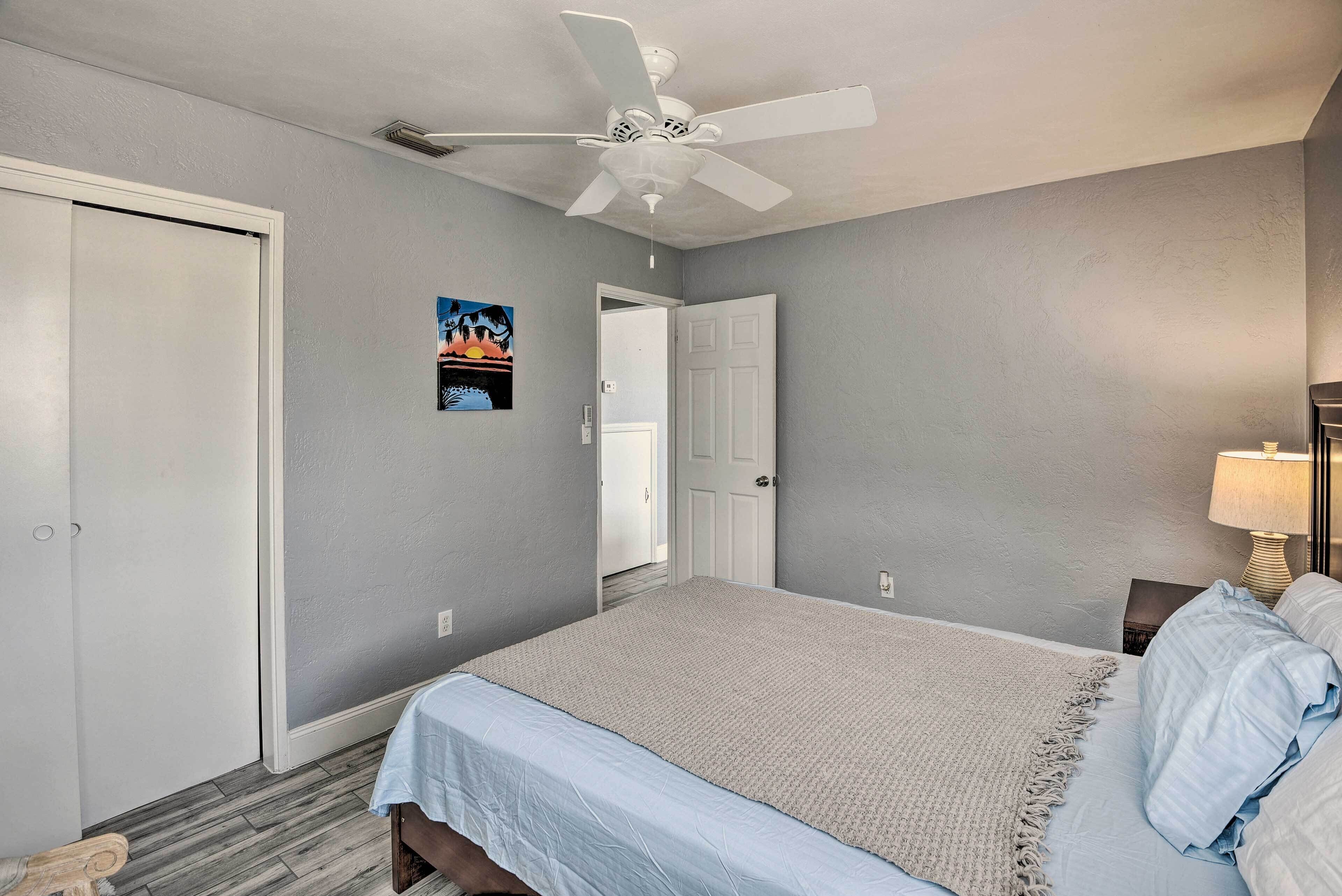 A bedroom with a bed, a ceiling fan, a door, and a nightstand with a lamp.