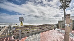Een vogelvlucht over een looppad dat naar het strand leidt, met een bord, houten omheining en paaltjes.